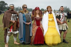 Three women dressed in medieval and princess costumes are between two men in roman uniforms.